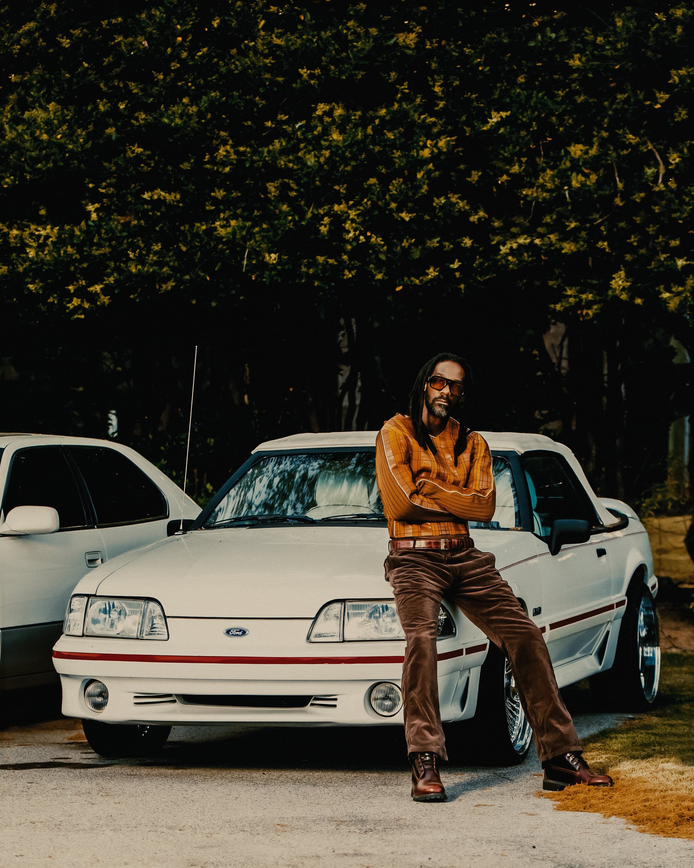 Shannon McCollum leaning against a vintage Ford Mustang at dusk, arms crossed