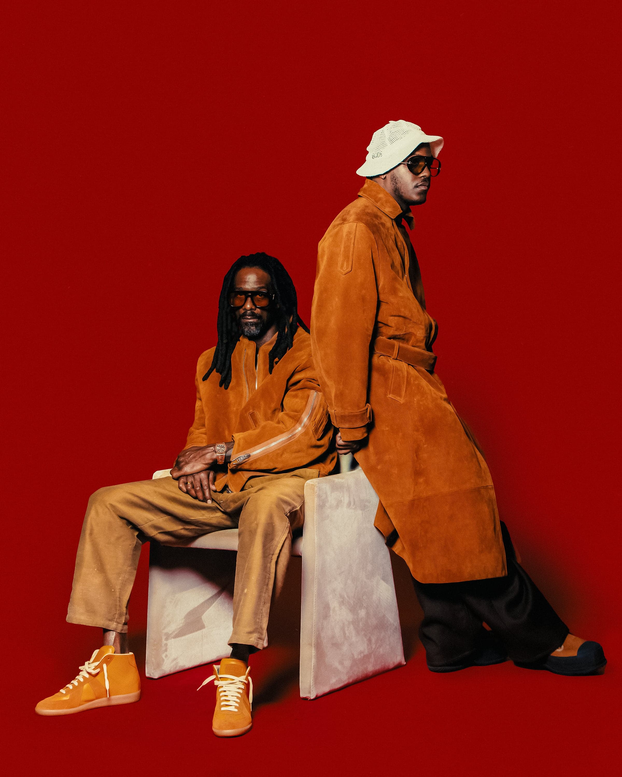 Lil Yachty and Shannon McCollum in matching orange suede, Shannon seated on a white block, red seamless